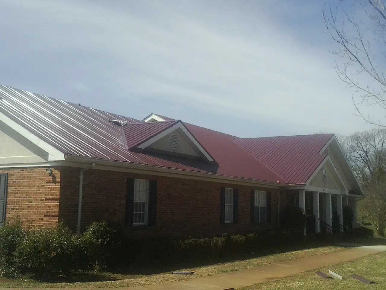 Red metal roof with gabled entries on a long brick building, from a Hail Damage Roof Repair job in Preston