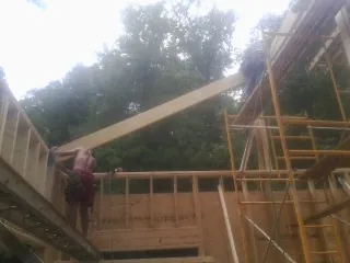 Carpenter raising a rafter beam on a new second story frame in Preston