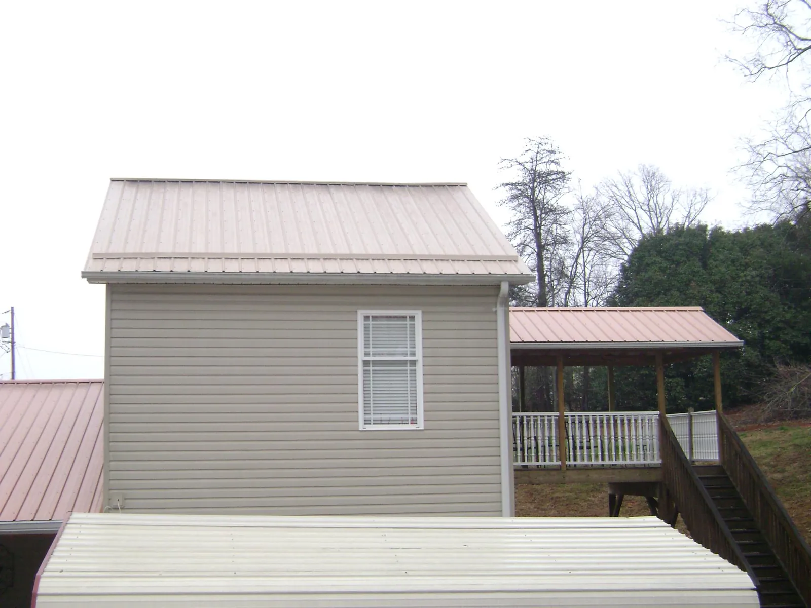 Tan metal roofs on a two story addition and attached porch, from a Roof Replacement job in Preston